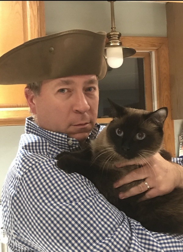 A man holding a siamese cat in a hat.