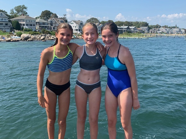 Three girls in swimsuits standing on a dock.