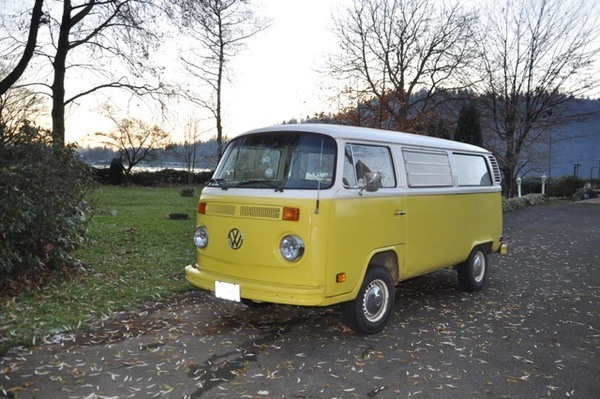A yellow and white vw bus parked on the side of the road.