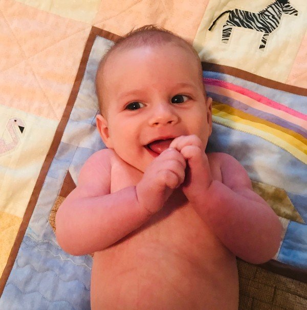 A baby smiles while laying on a quilt.