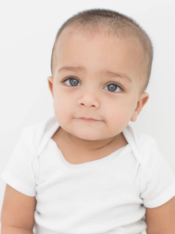 A baby with blue eyes is sitting on a white background.