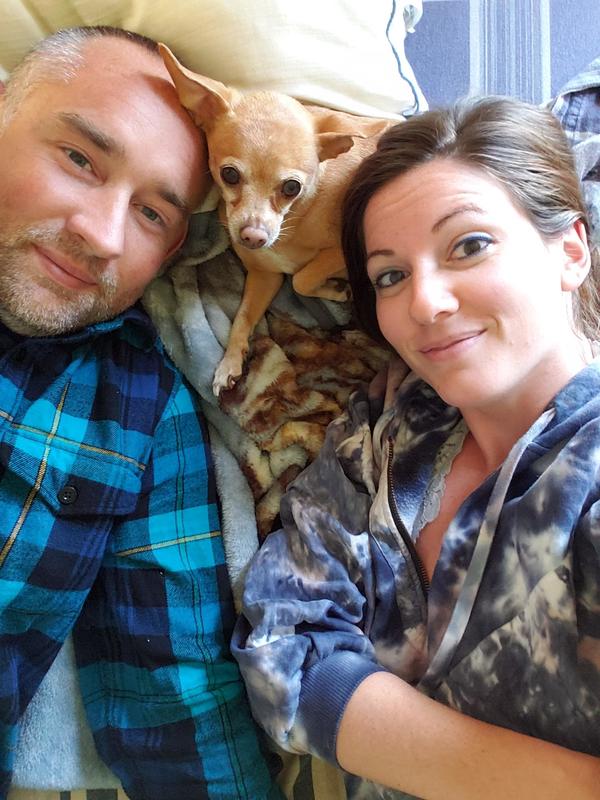 A man and woman laying on a bed with a chihuahua dog.