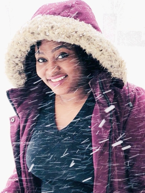 A woman in a burgundy jacket smiling in the snow.