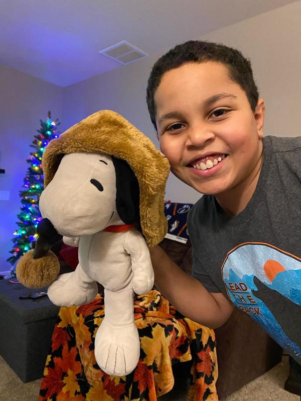 A boy holding a snoopy stuffed animal in front of a christmas tree.
