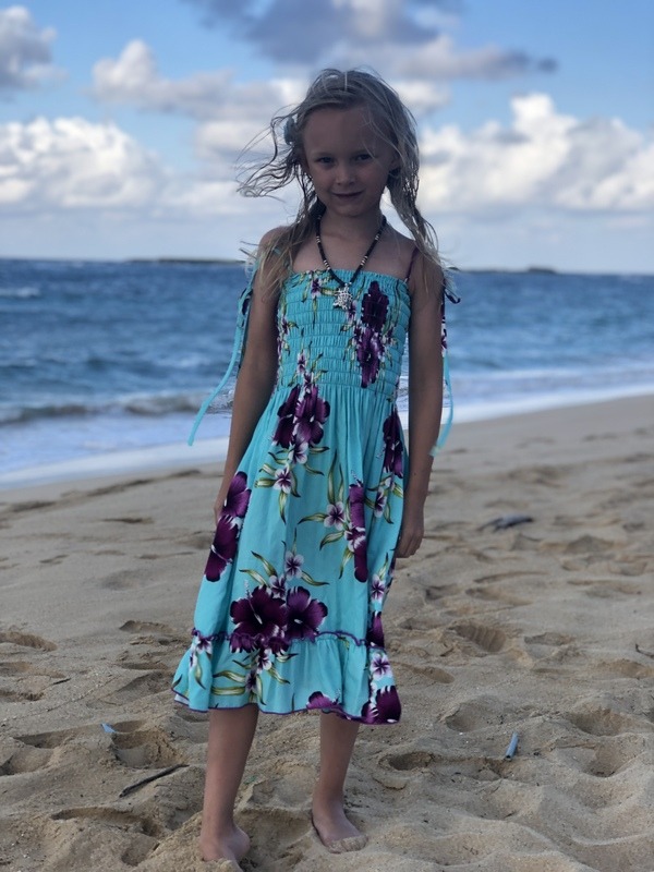 A little girl standing on the beach in a floral dress.