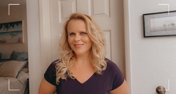 A woman in a purple shirt standing in front of a door.