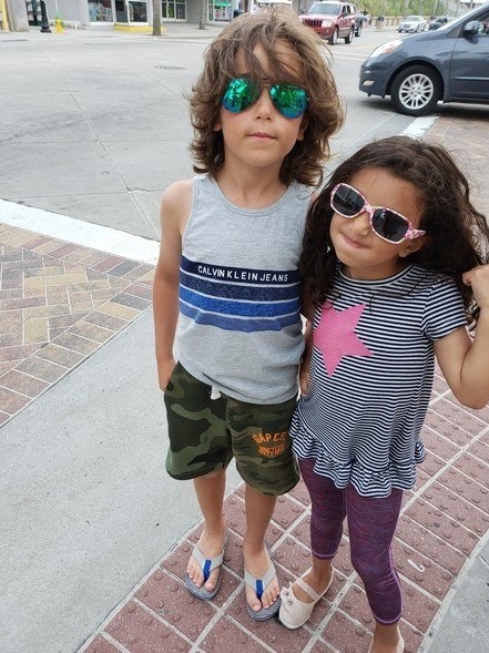 Two kids wearing sunglasses on a sidewalk.
