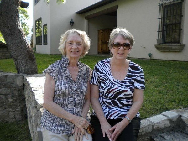 Two older women posing for a picture in front of a house.