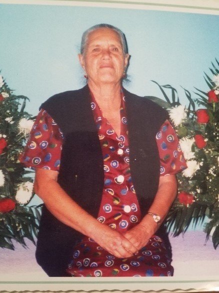 A photo of an older woman sitting in front of flowers.