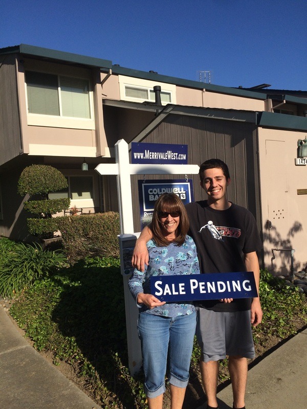 Two people standing in front of a house with a sale pending sign.
