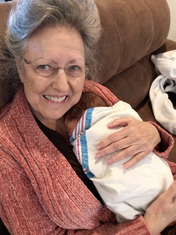 An older woman holding a baby on a couch.