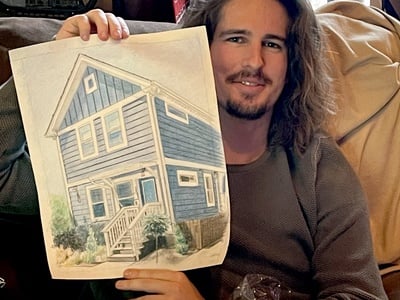 A man showcasing a colored pencil portrait of a house, created by a portrait maker.
