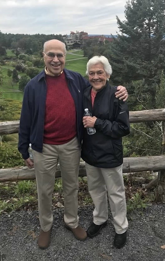 An older couple posing for a photo in front of a golf course.
