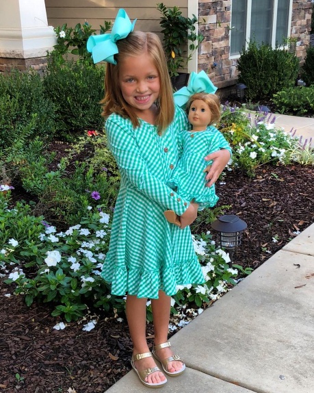 A little girl holding a doll in a green dress.