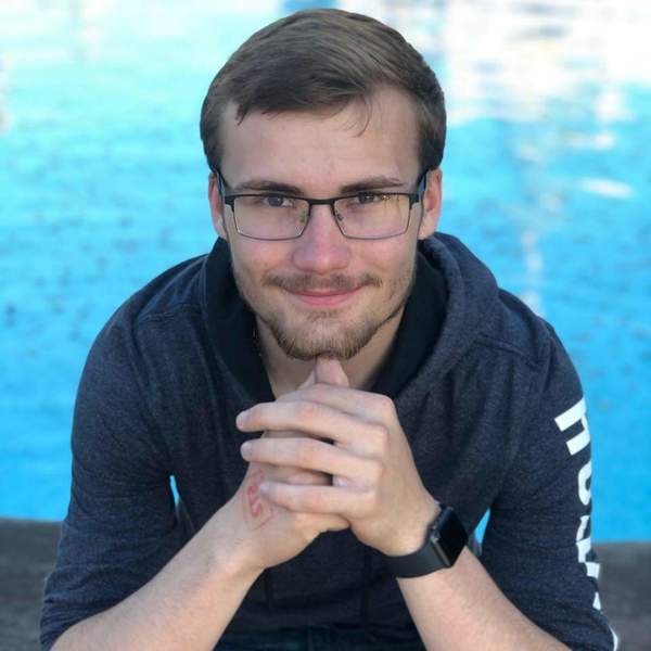 A young man with glasses sitting by a pool.