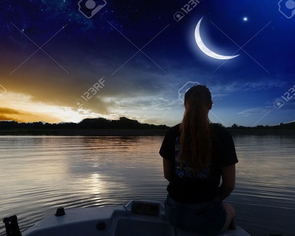 A girl sitting on a boat looking at the moon and crescent stock photo.