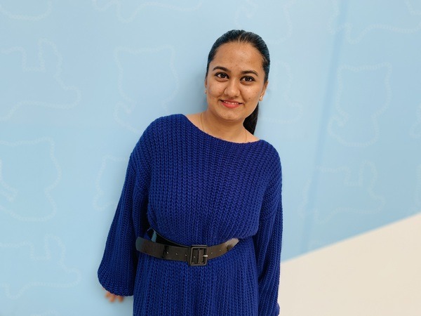 A woman in a blue sweater standing in front of a blue wall.