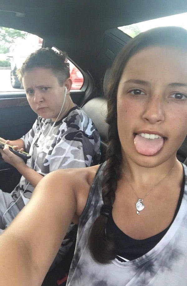 Two girls sitting in the back seat of a car with their tongues out.
