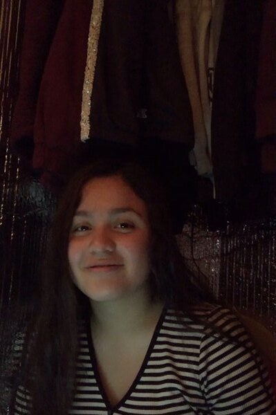 A girl sitting in front of a rack of clothes.