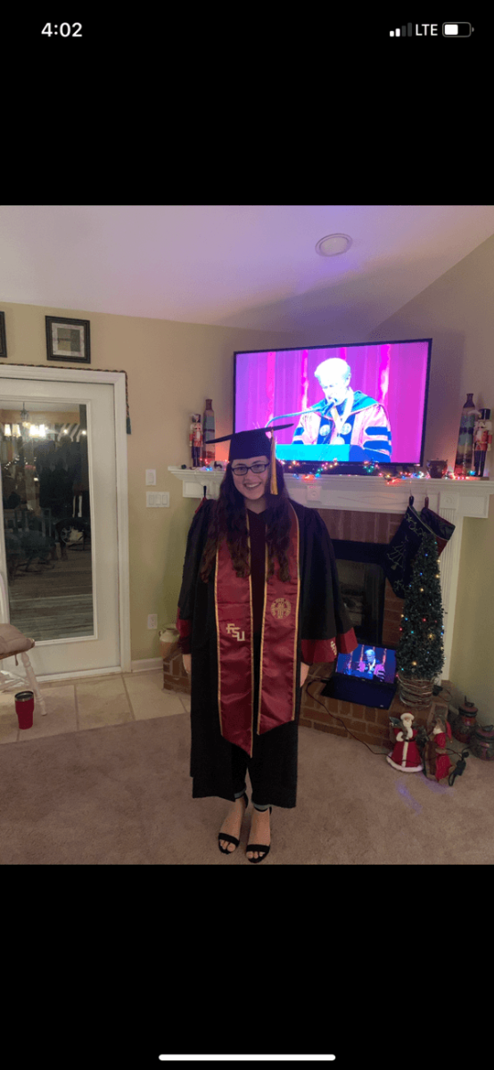 A woman in a graduation gown standing in front of a tv.