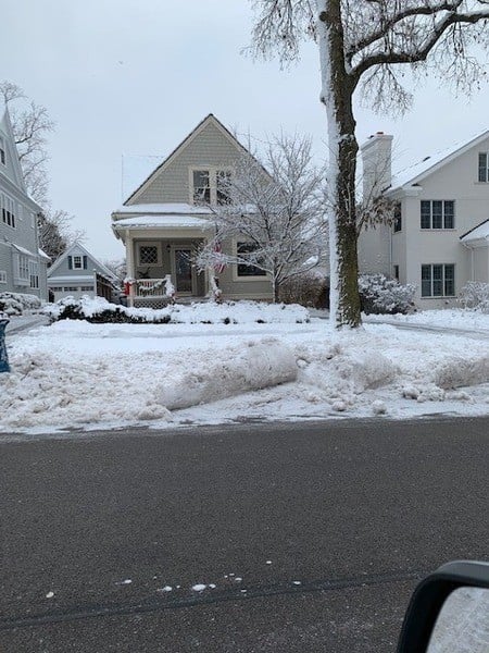 A snowy street with a car parked in front of a house.