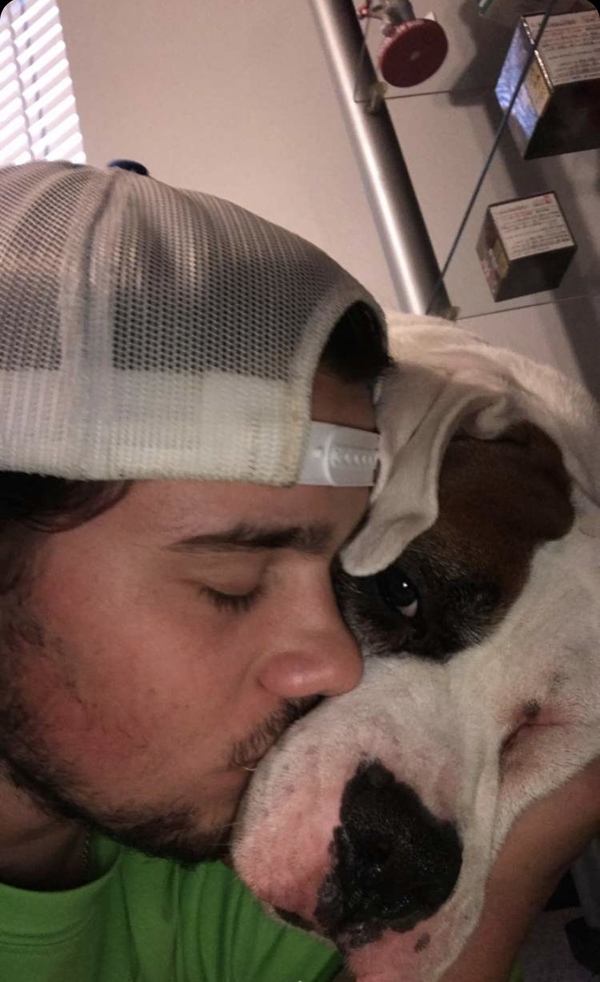 A man kissing his dog in a hat.