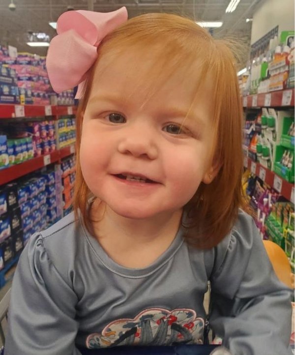 A little girl with red hair sitting in a grocery store.