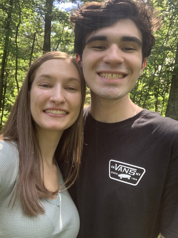 A man and woman smiling in the woods.