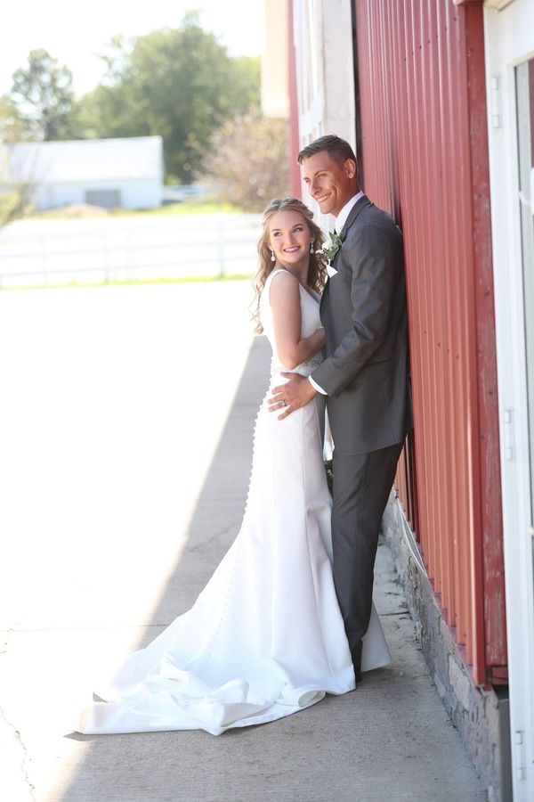 A bride and groom posing in front of a barn.