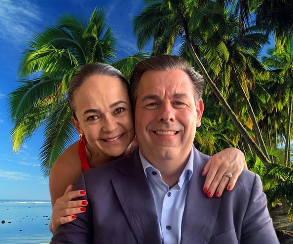 A man and woman posing in front of a palm tree.