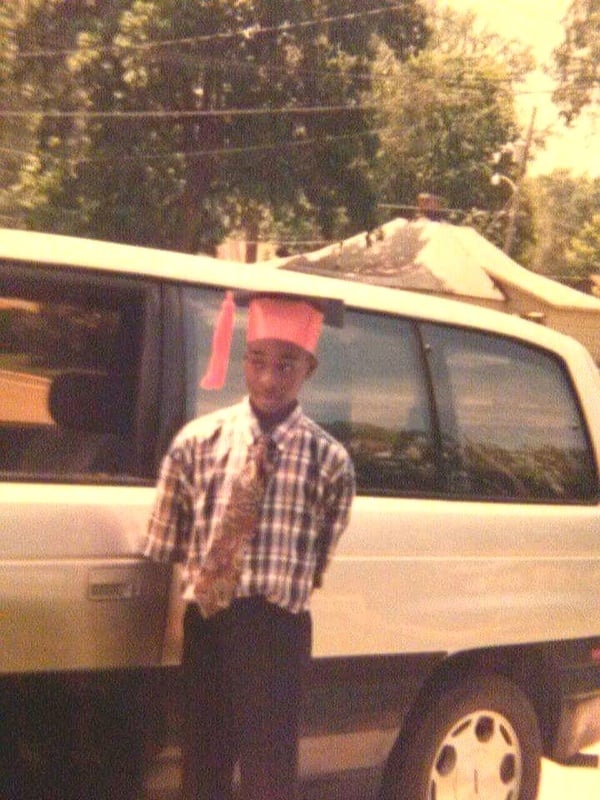 A boy in a graduation hat standing next to a suv.