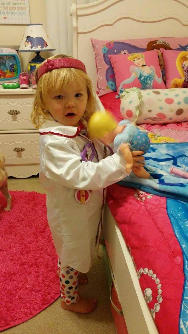 A little girl dressed as a doctor in a pink lab coat.