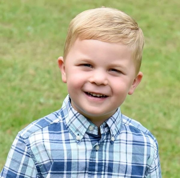 A young boy in a plaid shirt is smiling.