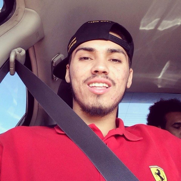 A man in a red shirt sitting in the back seat of a car.