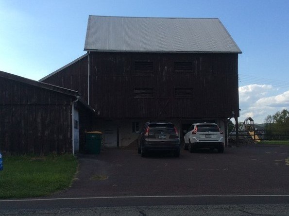 A barn with two cars parked in front of it.