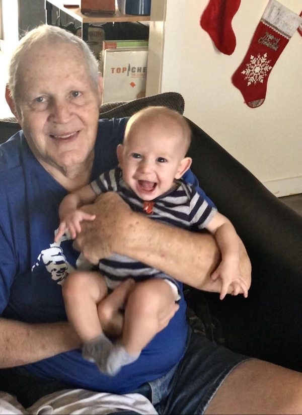 An older man holding a baby on a couch.