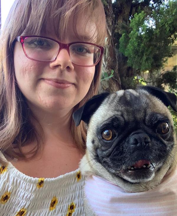 A woman wearing glasses and a bandana with a pug.