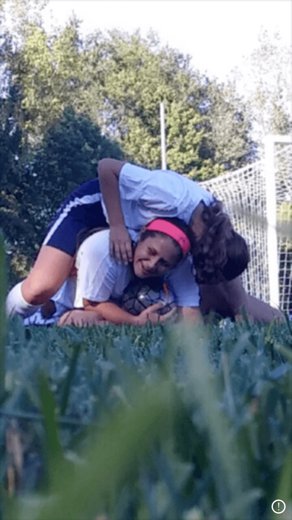 Two girls are laying on the ground in a soccer field.