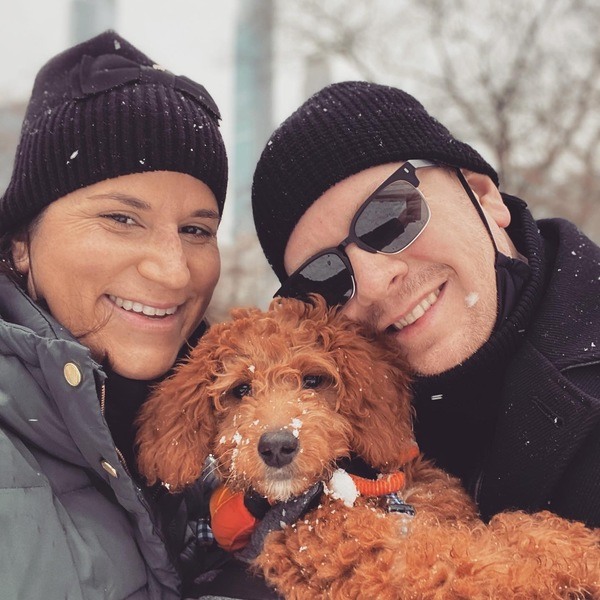 A man and woman are posing with their dog in the snow.