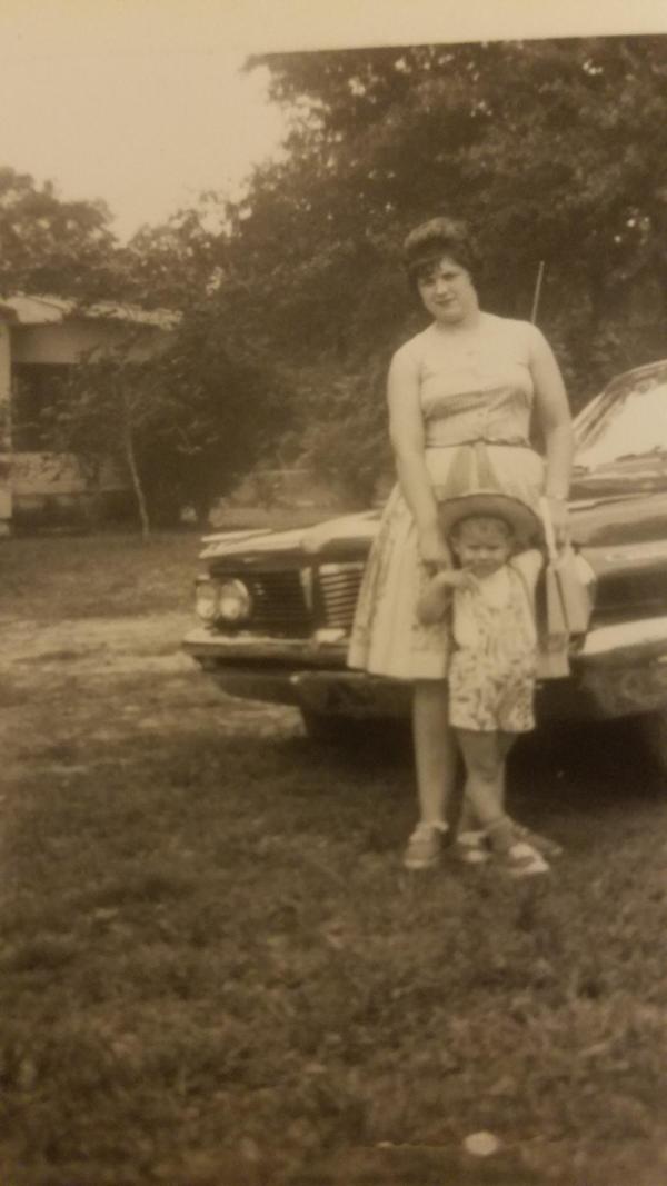 An old photo of a woman and child standing next to a car.
