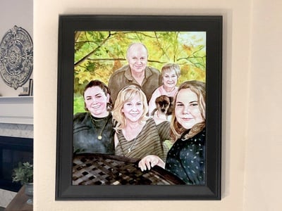  A framed watercolor portrait of a family, made from a reference photo, hung on a wall in front of a fireplace.